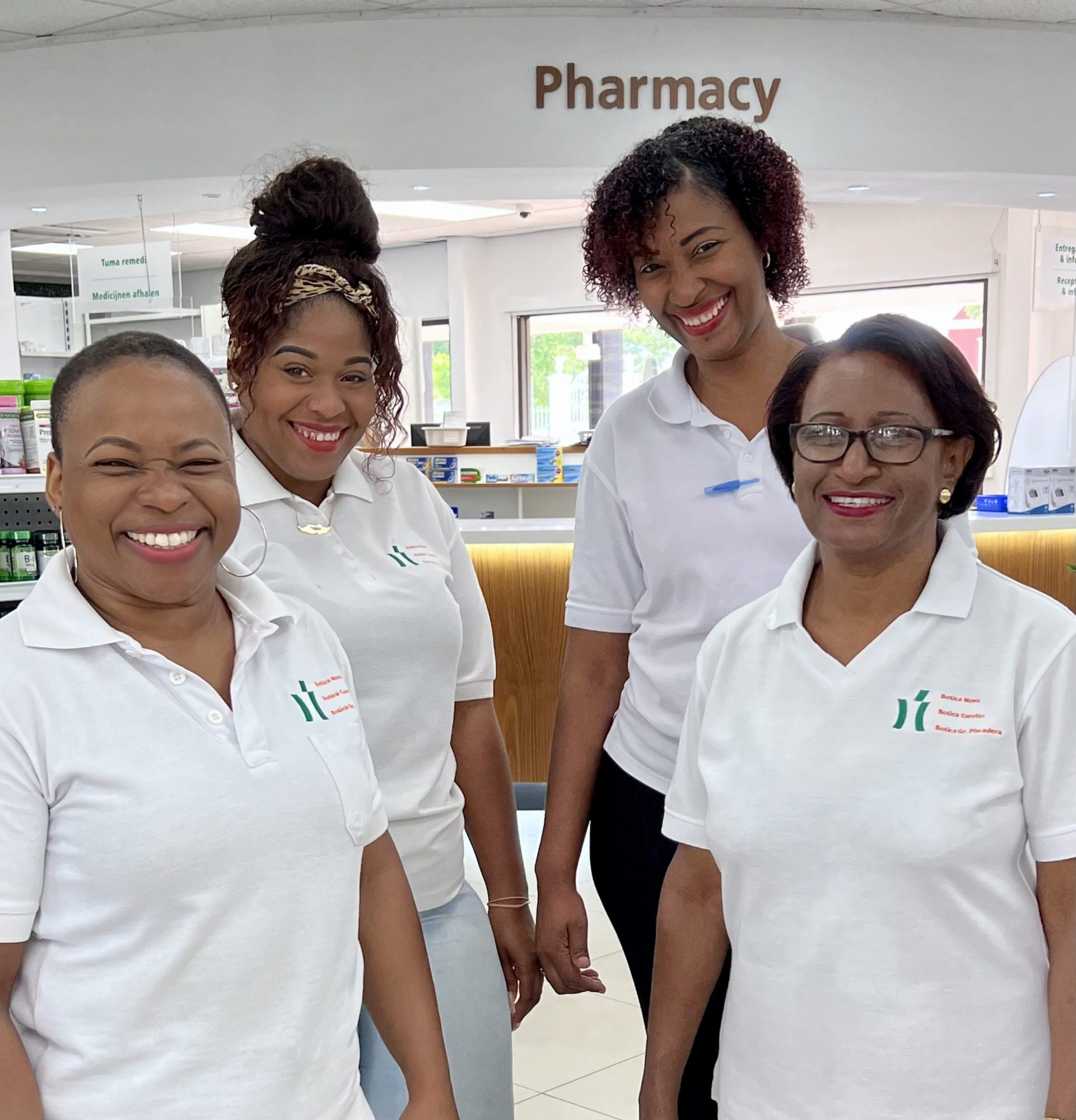 Four woman in the pharmacy wearing work clothing looking at the camera
